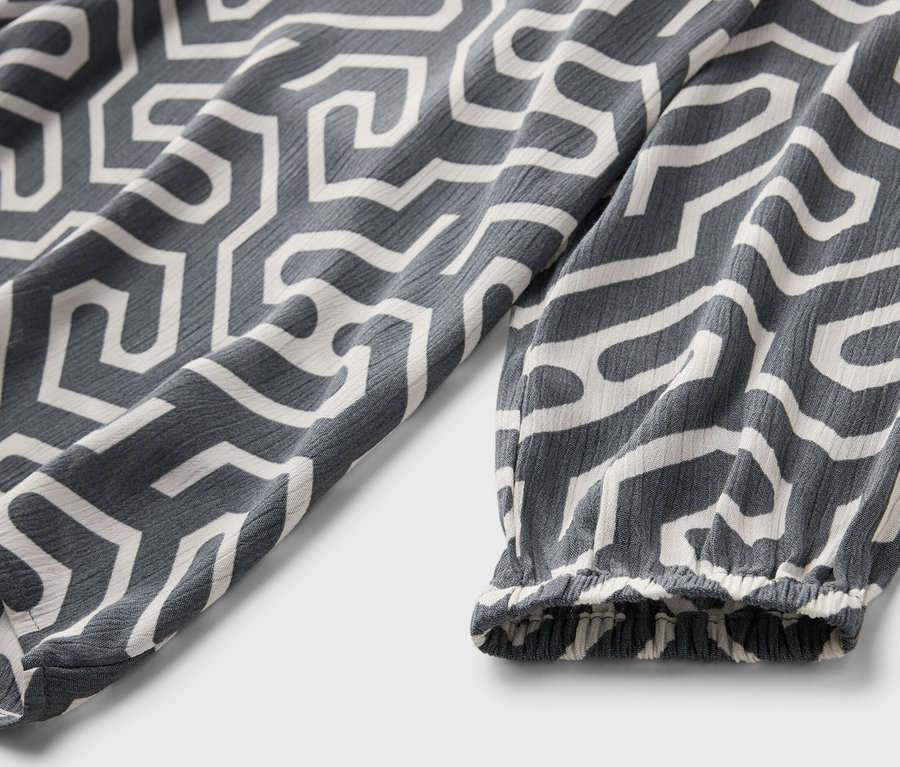 Detailansicht einer grauen Bluse in Crinkle-Optik mit weißem geometrischen Muster.