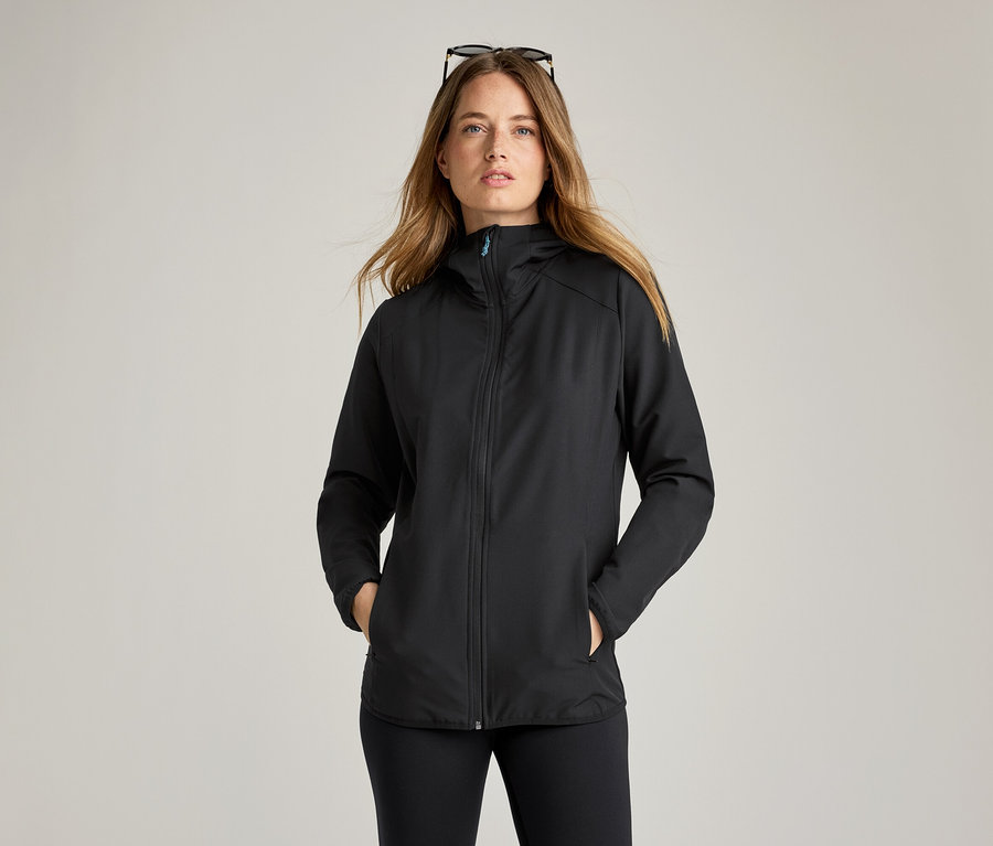 Frau mit Sonnenbrille auf dem Kopf trägt eine schwarze Softshelljacke.