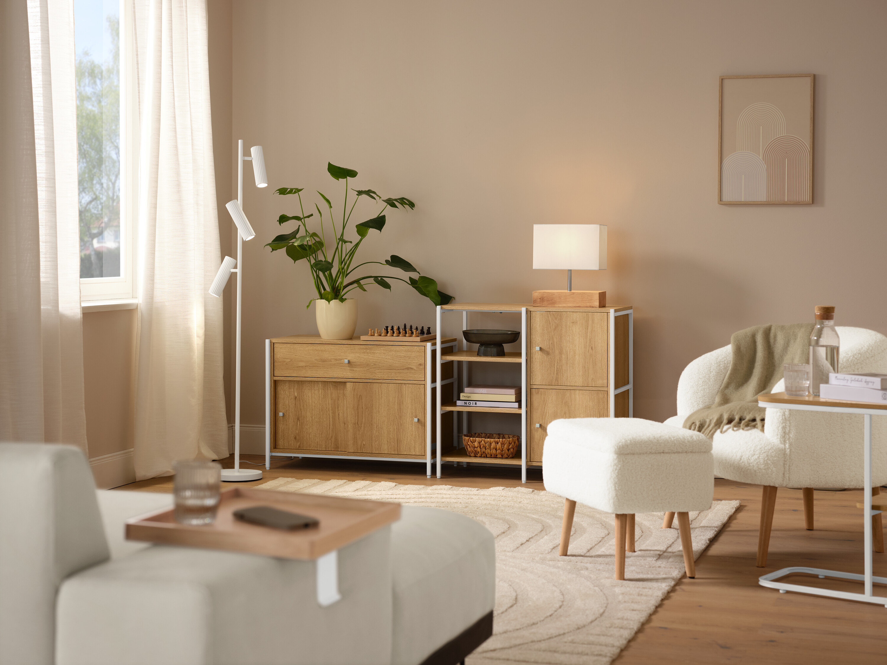 Einrichtungsszene mit einem beigen Teppich »Cosmo«, einem Bouclé-Sessel mit Holzbeinen, einem cremefarbenen DOMO Longchair, einer Trio Stehleuchte »Soka« und einer Tischleuchte mit Holzfuß.