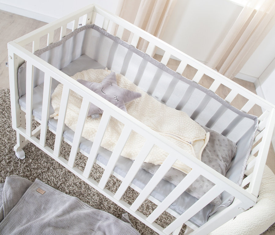 Weißes roba 3-in-1-Stuben-Beistellbett mit grauer Polsterung, Decke, Schlafsack und Sternkissen auf einem Teppich.