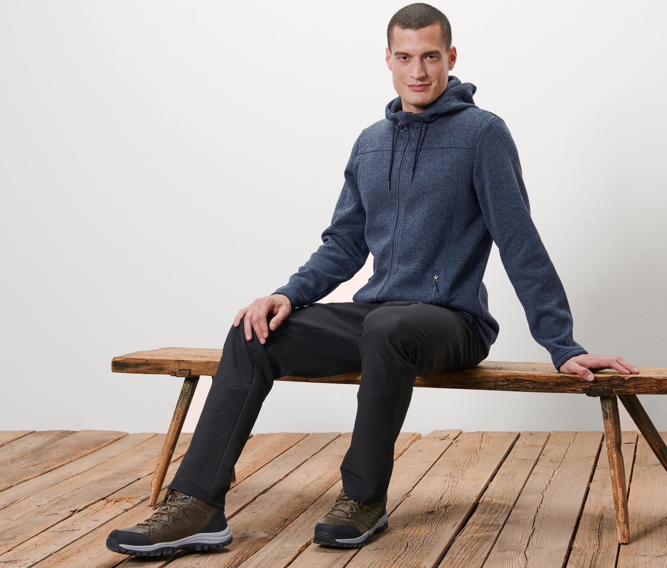 Mann sitzt auf einer Bank und trägt eine Strickfleece-Jacke.