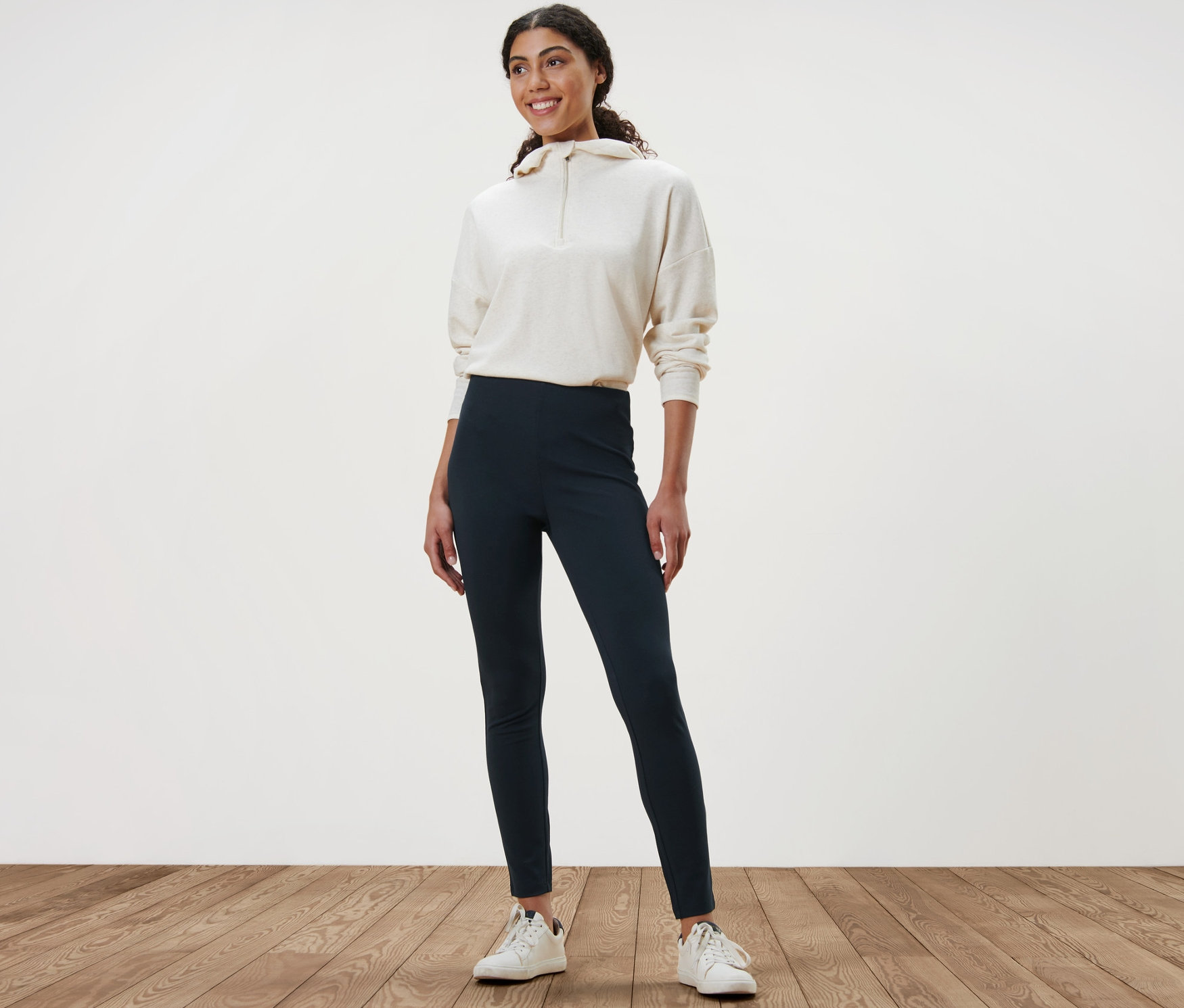 Eine Frau steht auf einem Holzboden und trägt Heavy-Leggings und ein Sweatshirt.