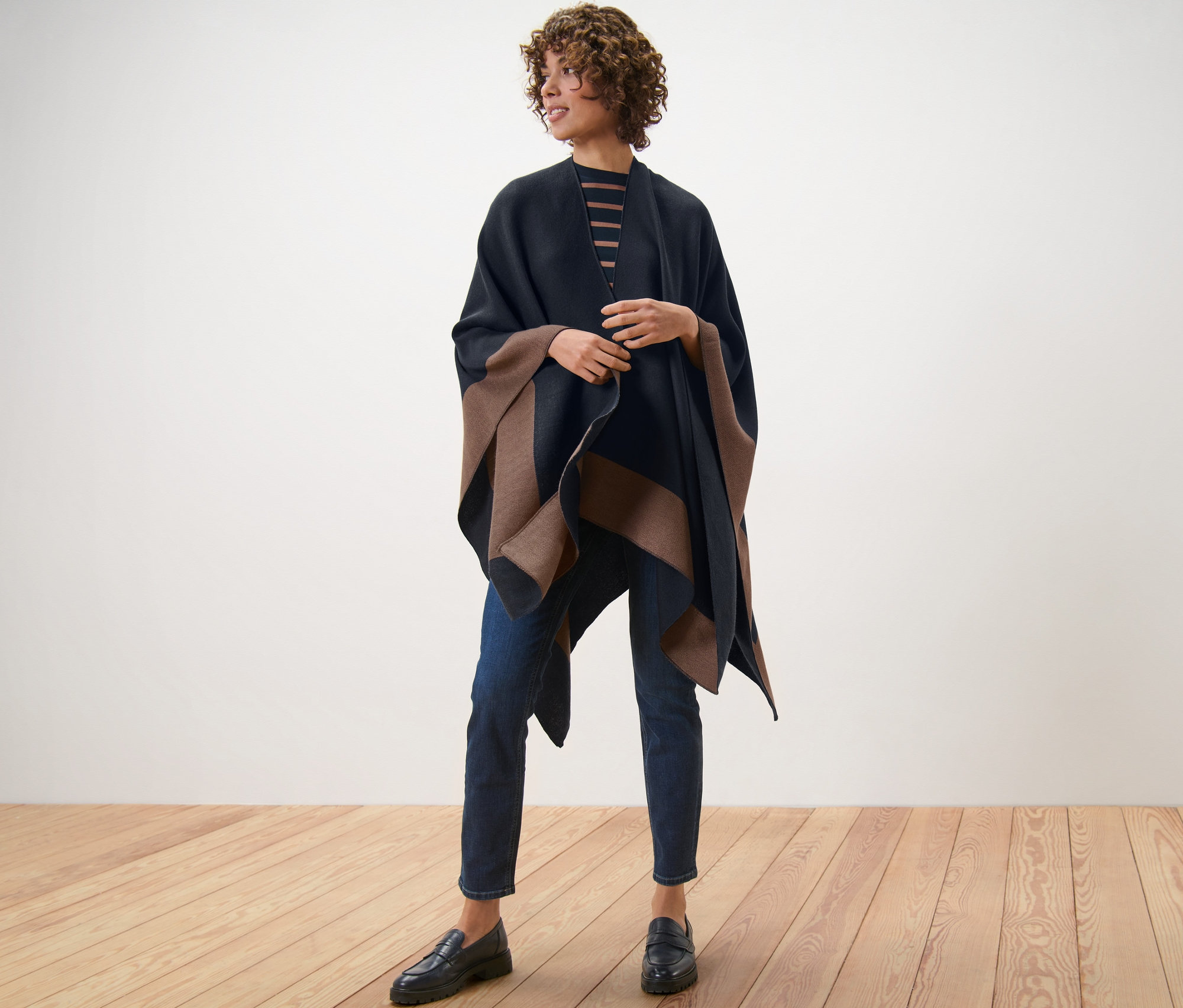 Eine Frau steht auf einem Holzboden und trägt einen Wende-Poncho.