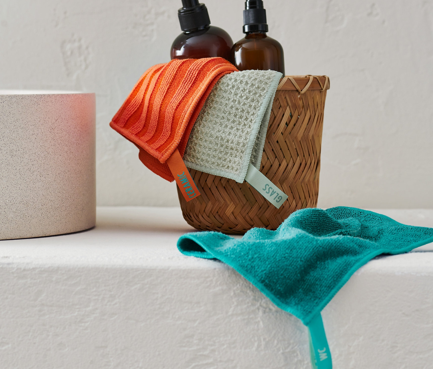 Reinigungstuch-Set liegt in einem Weidenkorb neben zwei braunen Flaschen.