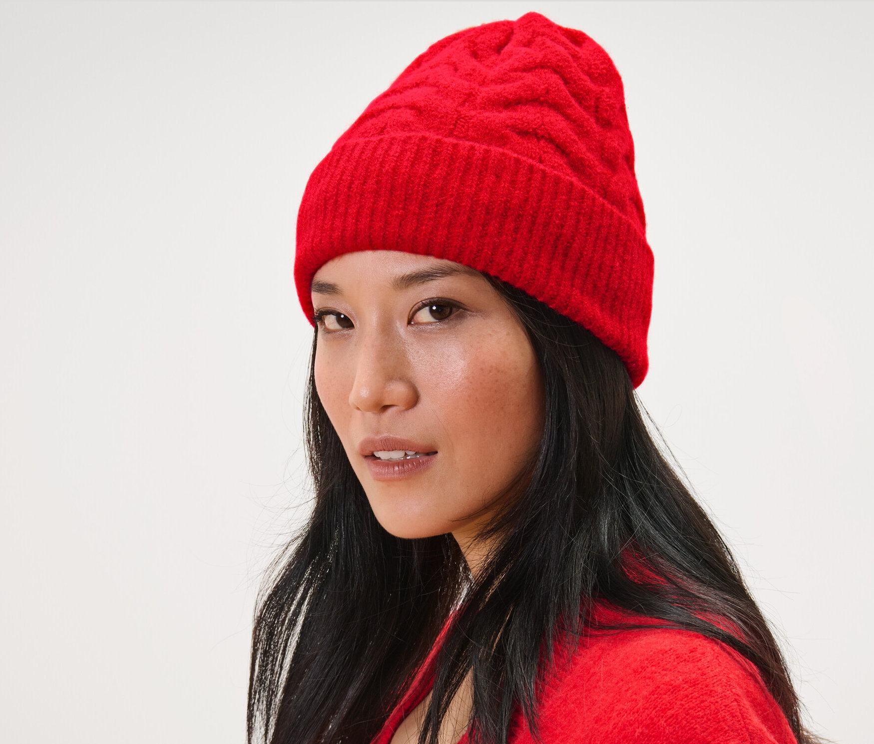 Frau mit dunklen Haaren trägt eine rote Strickmütze mit Zopfmuster und eine rote Strickjacke.