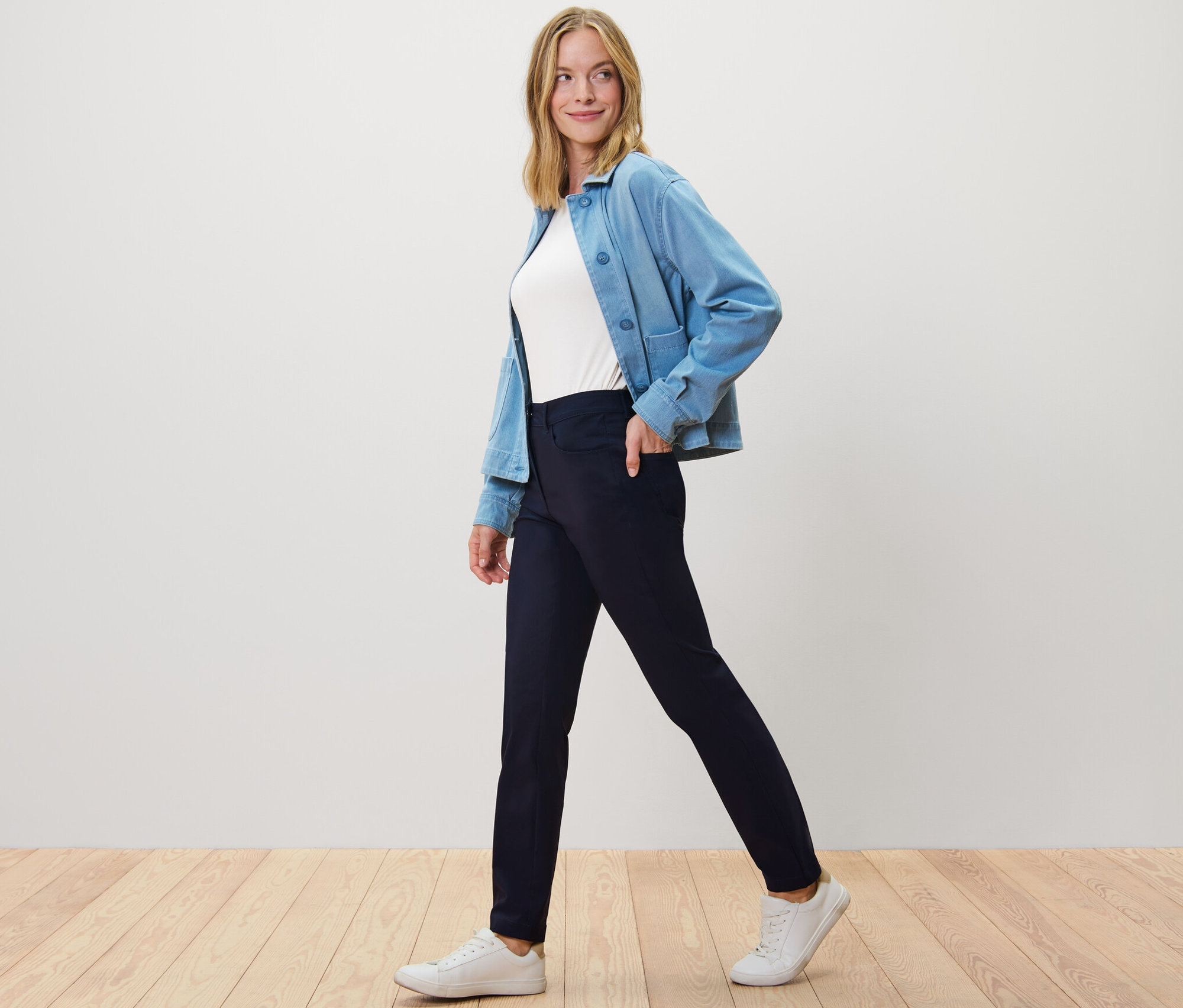 Frau geht, trägt dunkelblaue Bengalin-Hose, weißes T-Shirt und blaue Jacke.