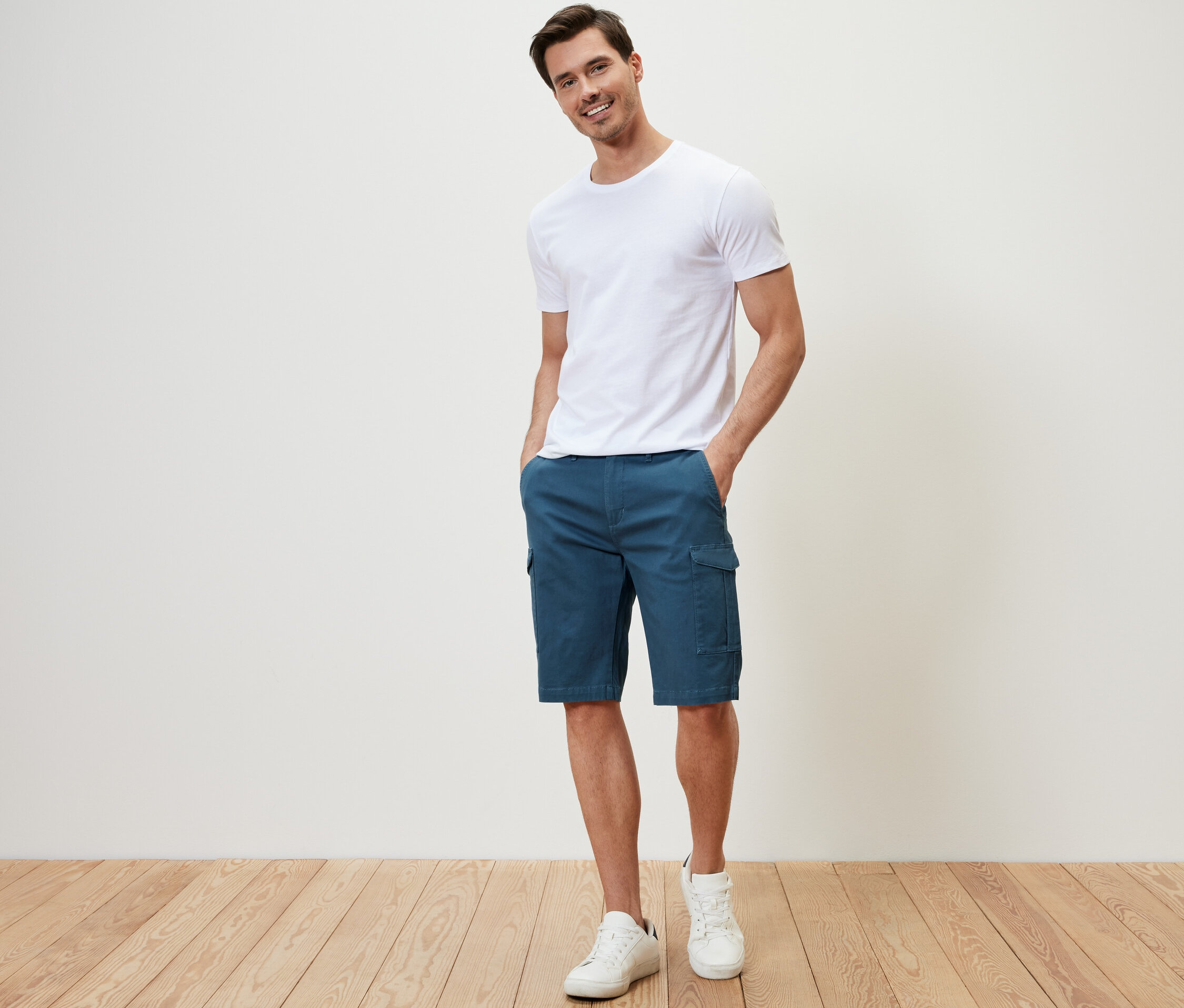Ein Mann steht mit den Händen in den Taschen seiner blauen Cargo-Shorts.