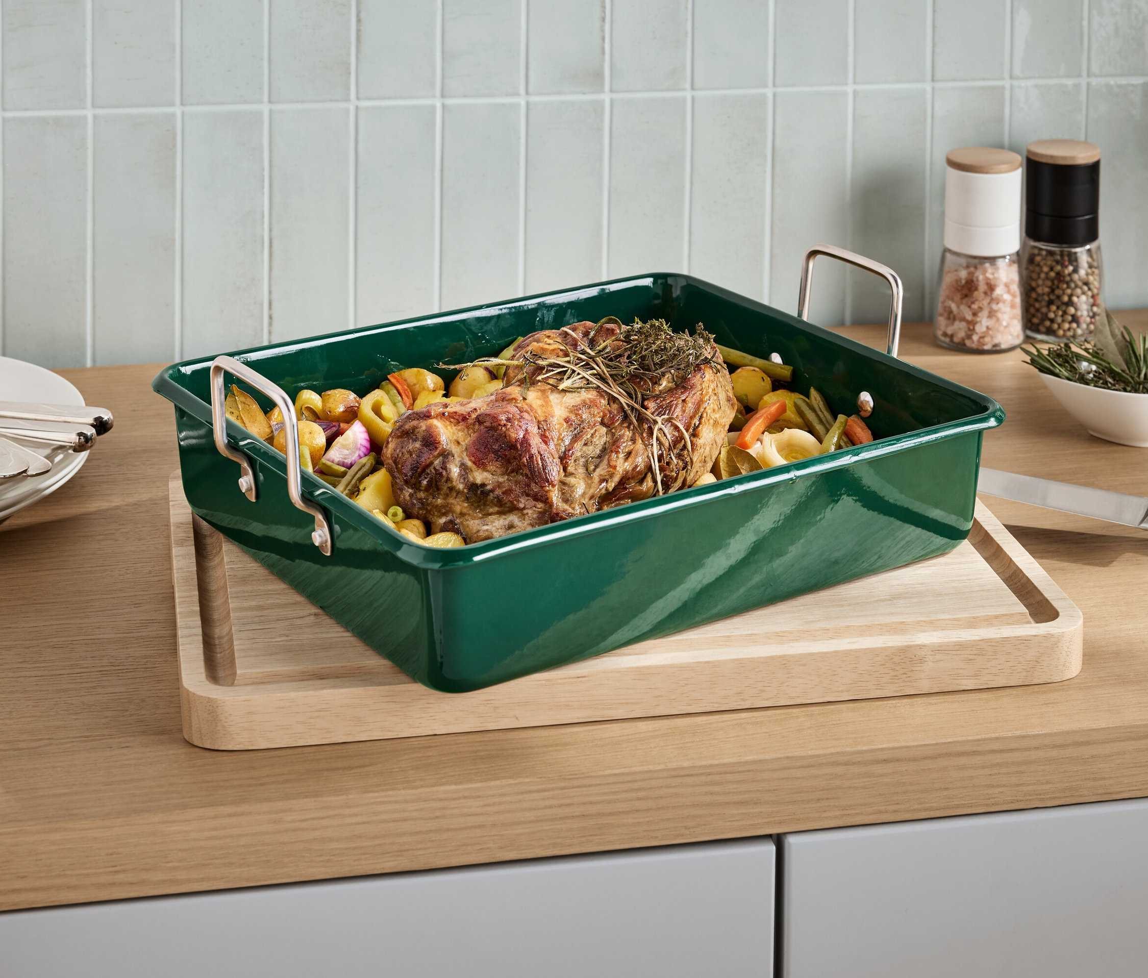 Braten mit Kräutern in grüner Bratform auf einem Brett.