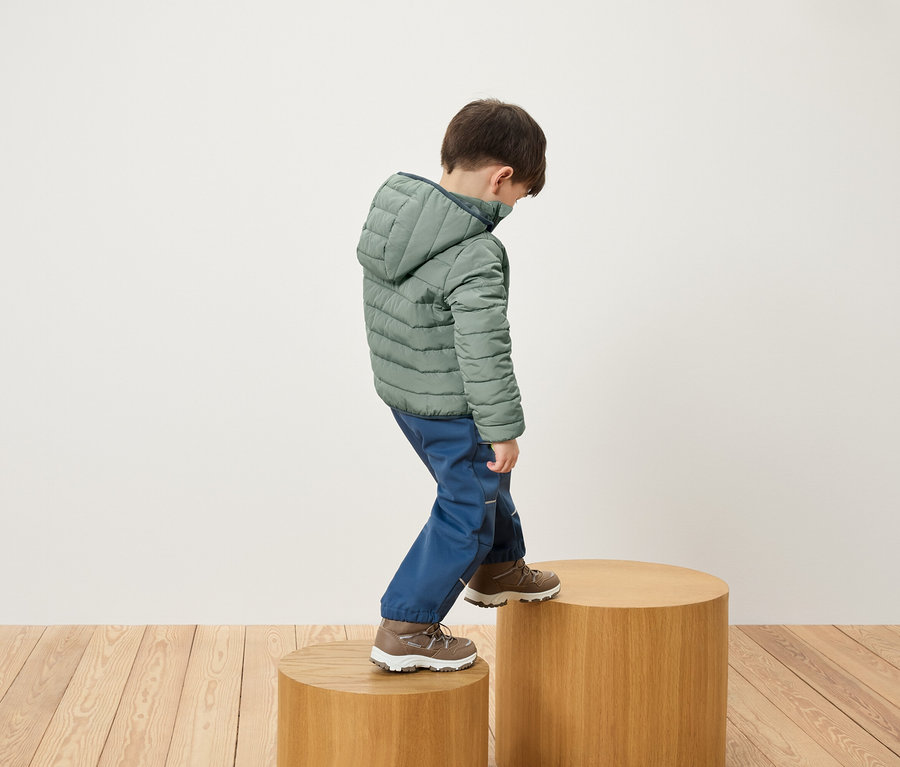 Junge in grüner Jacke und blauer Hose steigt auf ein Holzpodest.