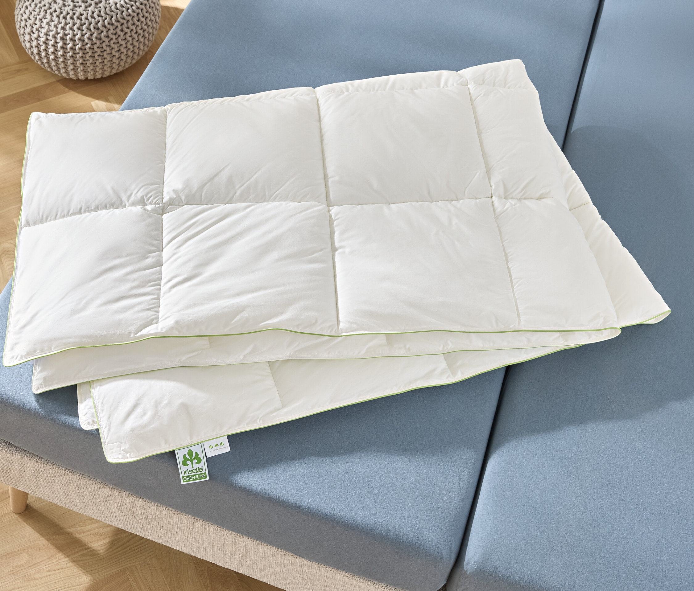 Eine gefaltete, weiße Steppdecke liegt auf einem blauen Bett.