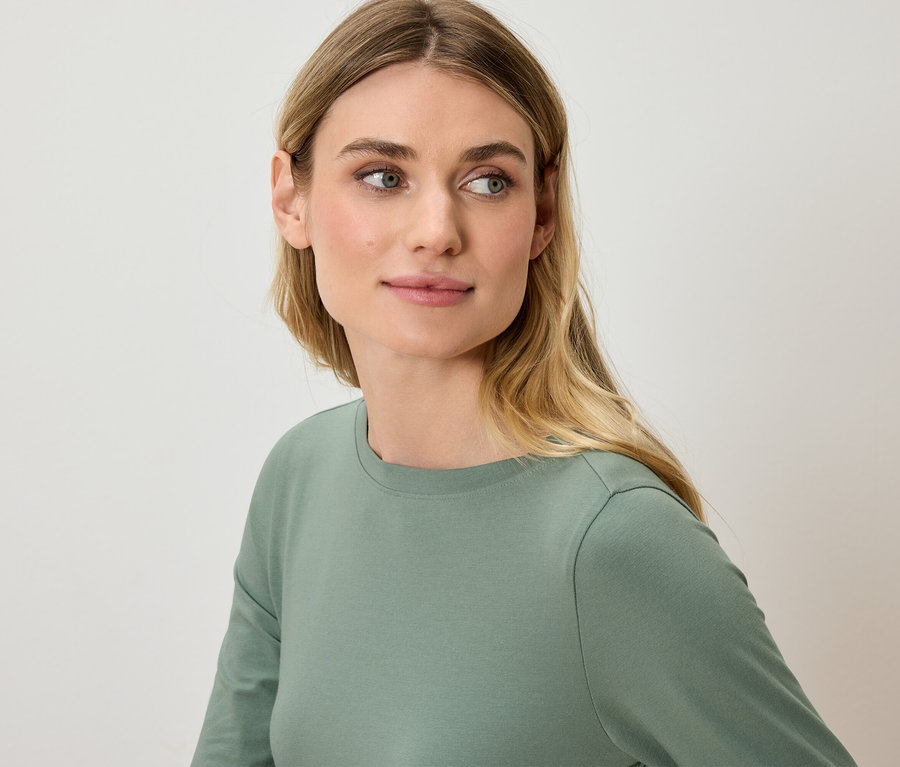 Porträt einer Frau mit blonden Haaren, die ein grünes Langarmshirt trägt.