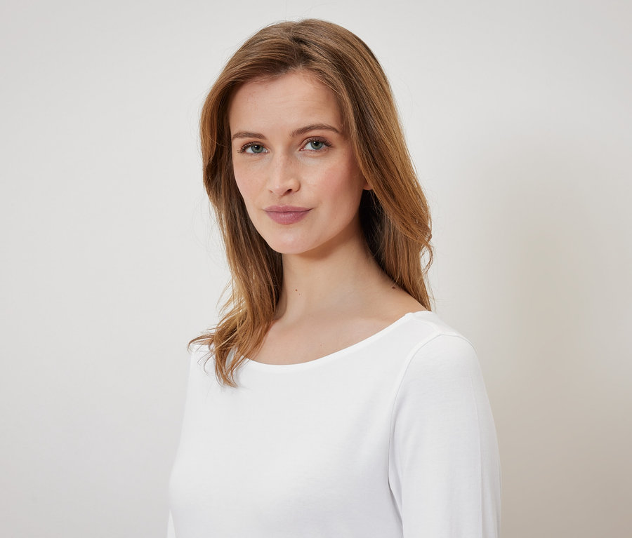 Porträt einer Frau mit braunen Haaren und blauen Augen in einem weißen T-Shirt.