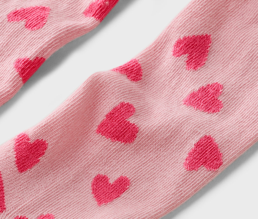 Nahaufnahme von hellrosa Socken mit roten Herzchenmuster.