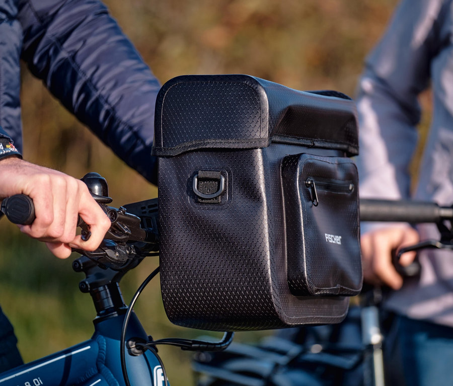 Nahaufnahme einer Person, die ein Fahrrad mit einer schwarzen FISCHER Lenkertasche PLUS+ Terra am Lenker fährt.