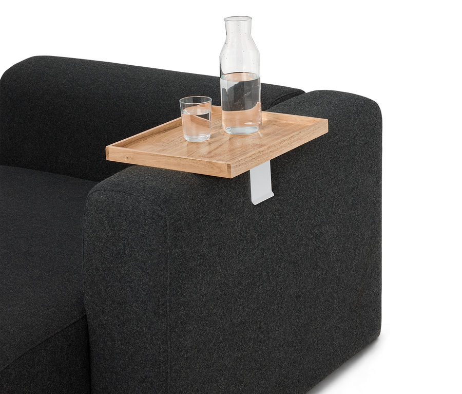 Auf einem grauen Sofa steht ein Holztablett mit einer Flasche und einem Glas Wasser.