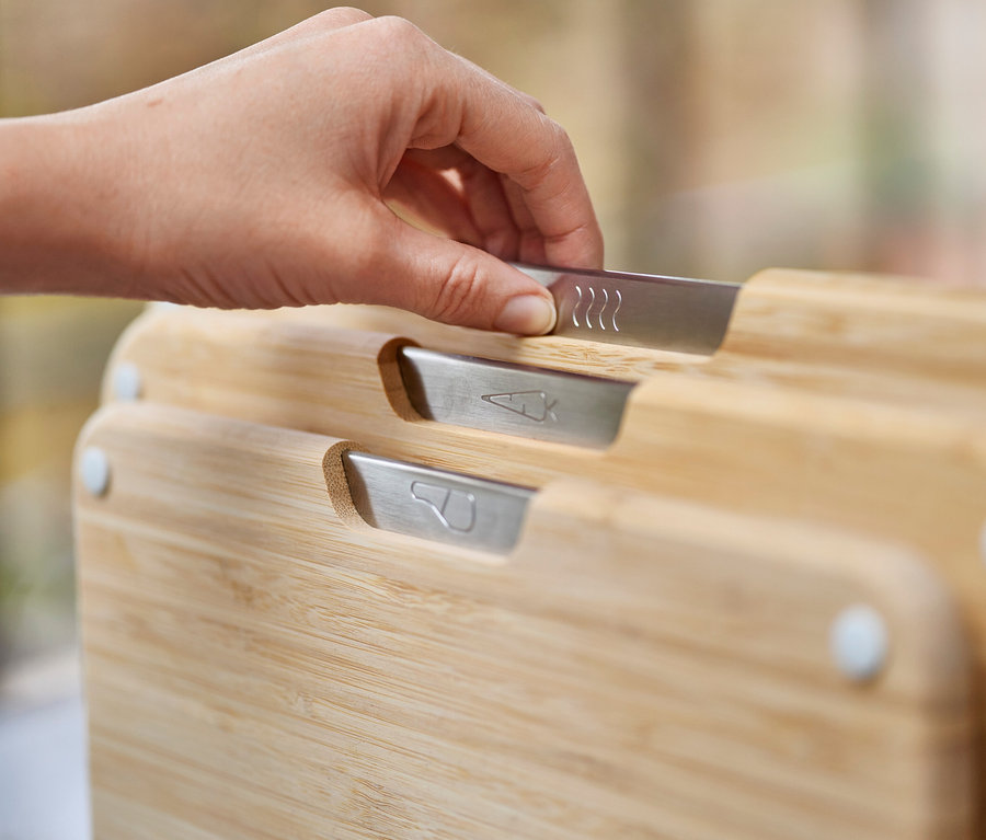 Eine Hand berührt den Griff eines Bambus-Schneidebretts mit einem Symbol für warme Speisen.