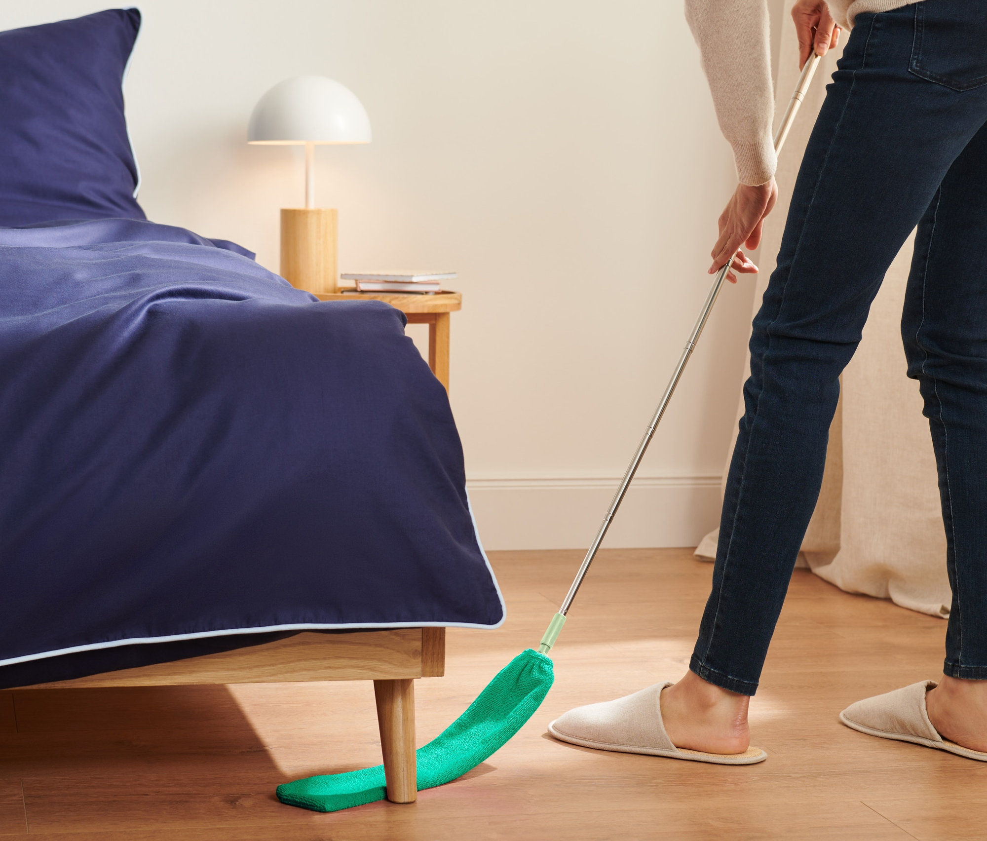 Frau wischt mit einem flexiblen Staubfänger unter dem Bett.