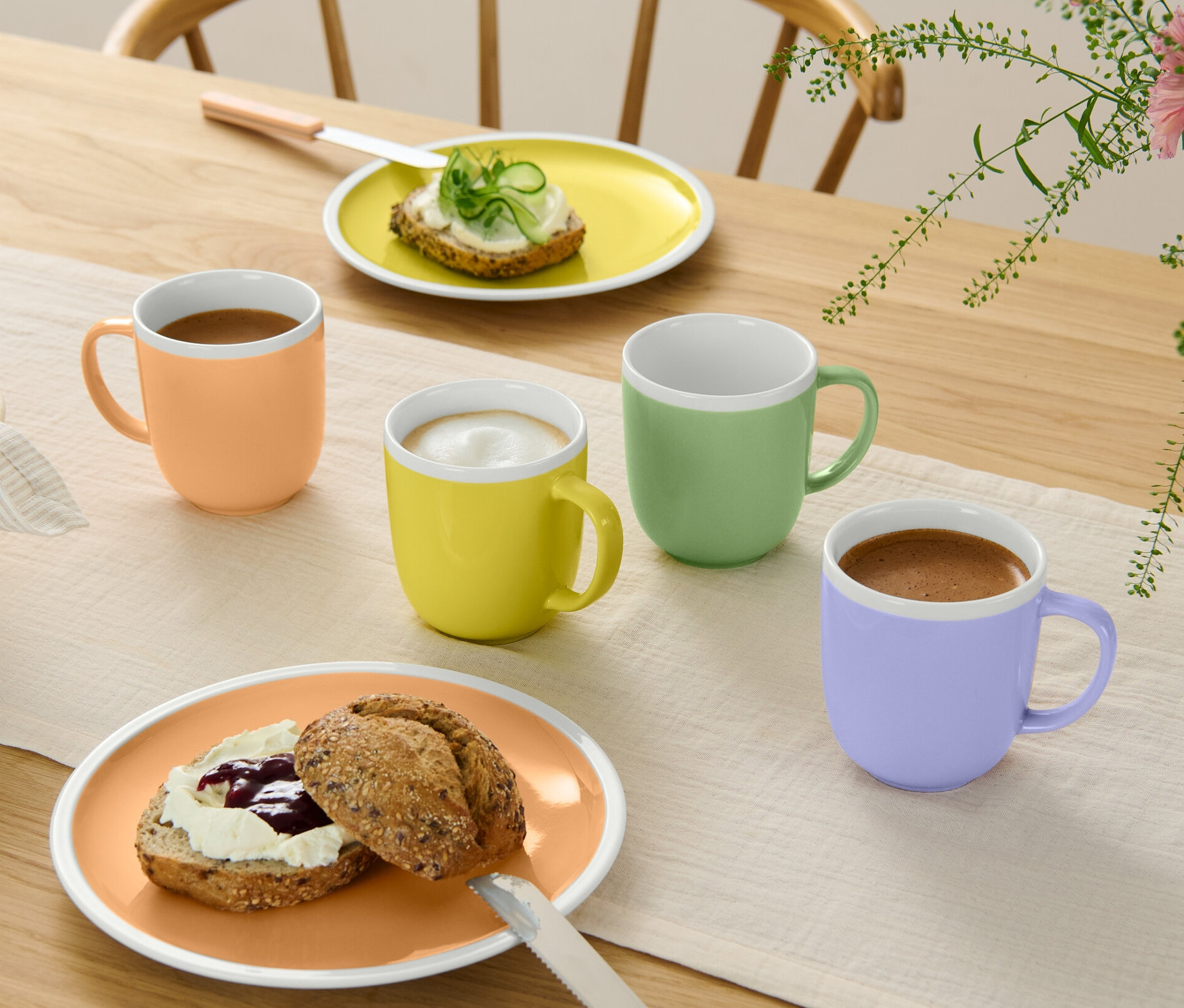Vier verschiedenfarbige Trinkbecher stehen neben Tellern mit Essen auf einem Tisch.