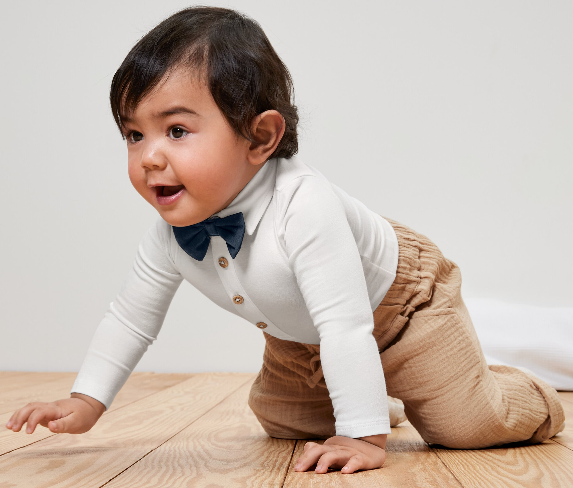 Baby krabbelt im Baby-Body mit Fliege auf einem Holzboden.