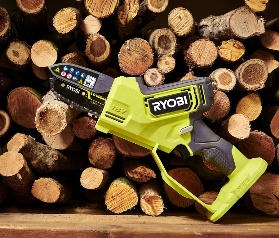 Eine hellgrüne Ryobi One+ Brushless Akku-Einhand-Kettensäge liegt auf einem Holzstapel.