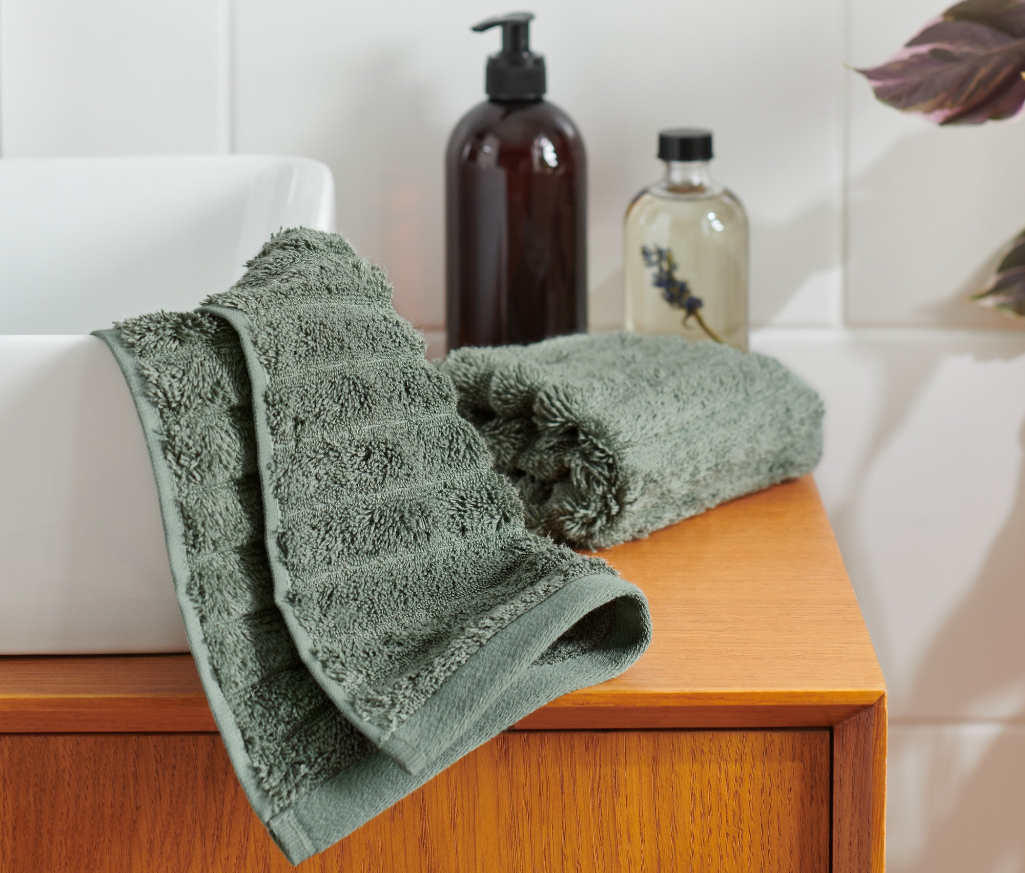Zwei grüne Premium-Gästehandtücher liegen neben einem Waschbecken auf einem Holzschrank.