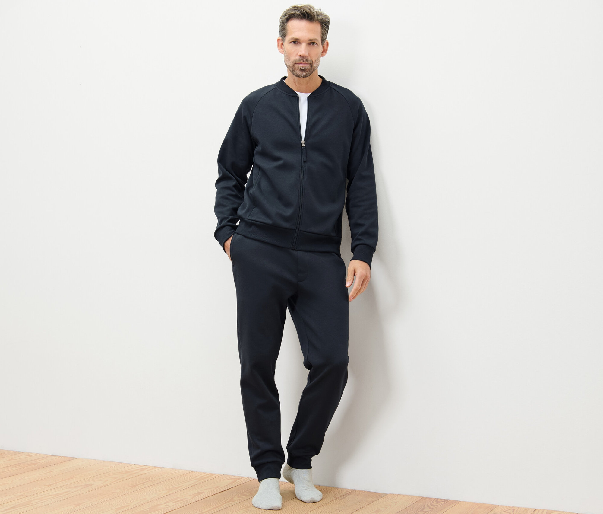 Mann posiert im dunkelblauen Hausanzug auf Holzboden.