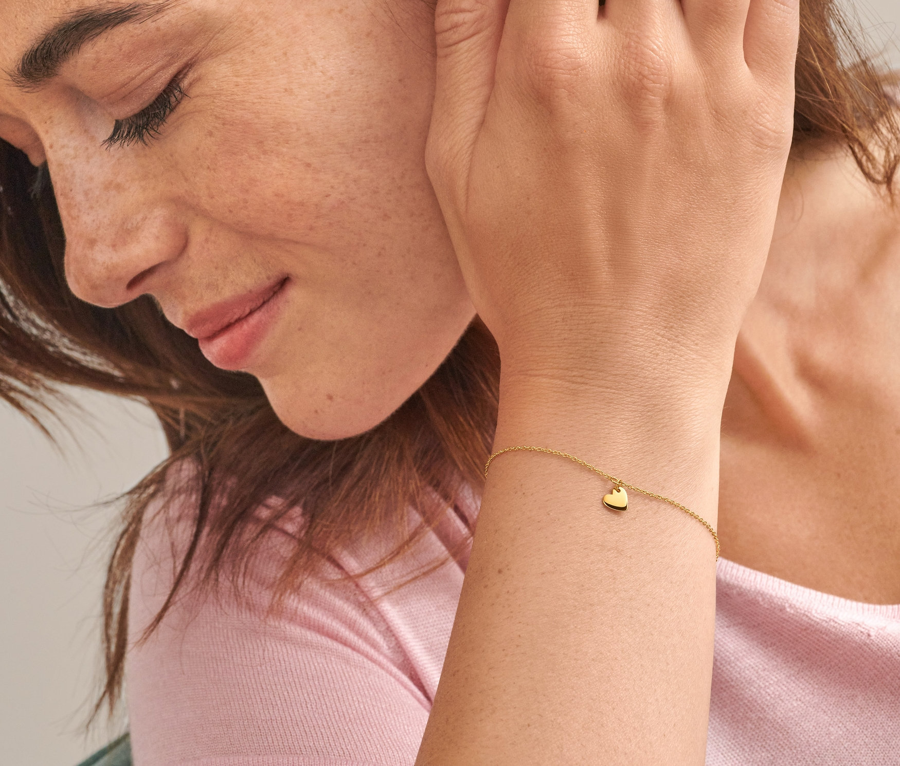 Nahaufnahme einer Frau mit braunen Haaren, die ein Gold-Armband mit Herzanhänger und einen Gold Ring V Zirkonia trägt.