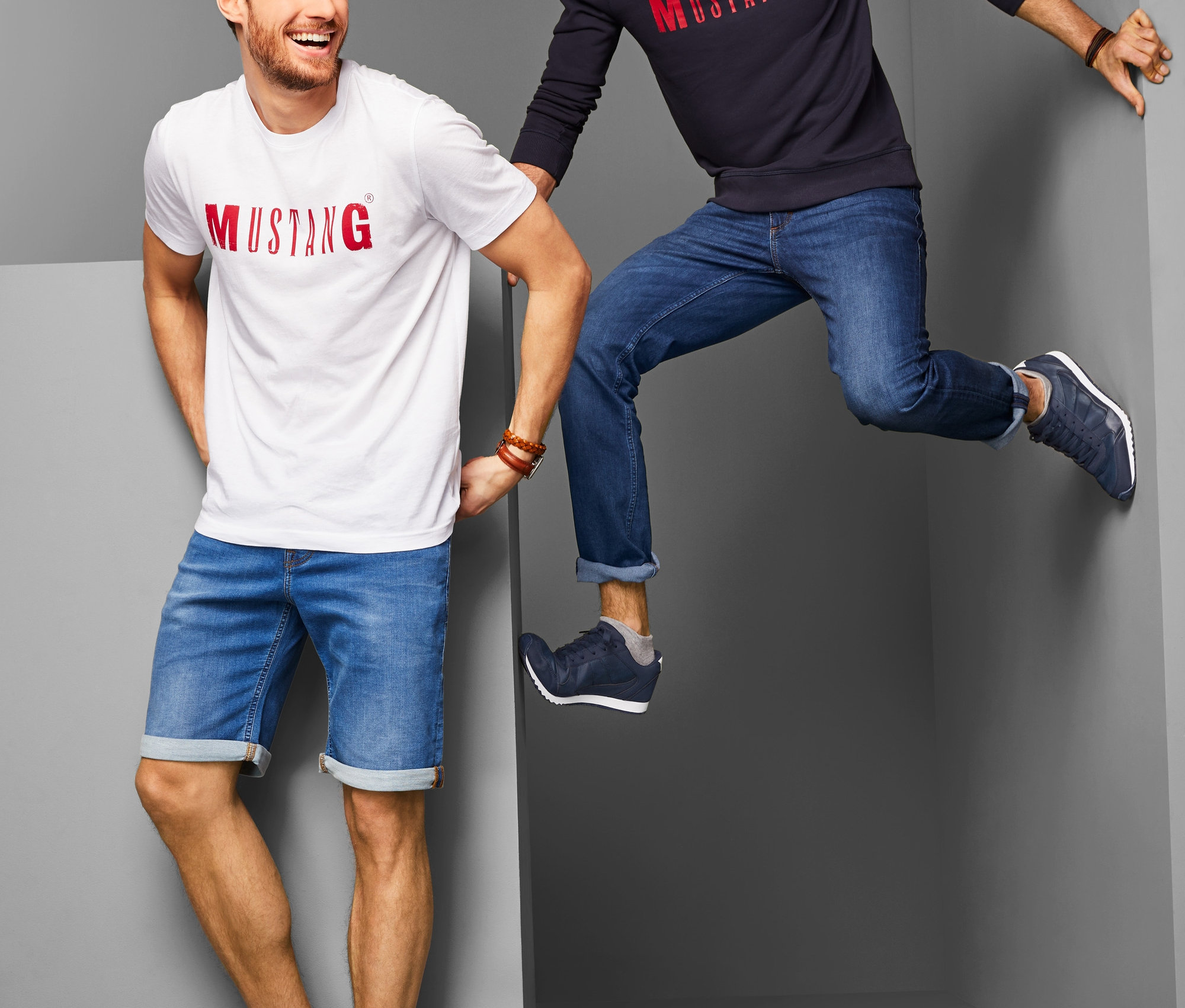 Zwei Männer posieren in Jeansshorts und Jeans und tragen Sneaker.