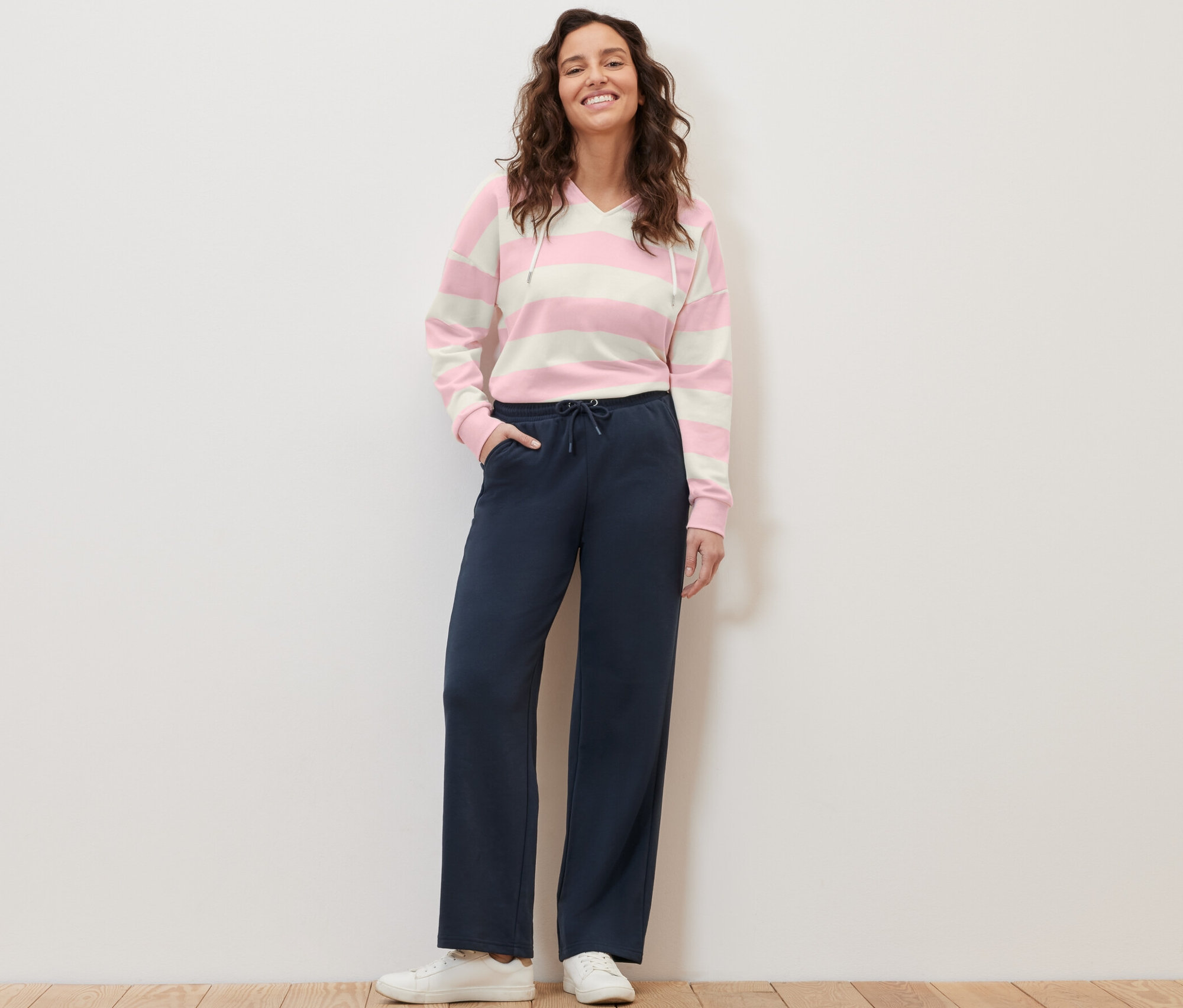 Eine Frau steht und posiert in dunkelblauen Sweathosen und einem gestreiften Hoodie.