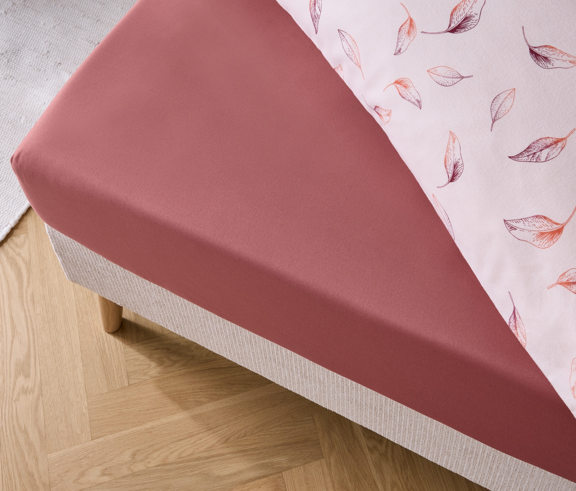 Detailansicht eines roten Spannbettlakens und eines Kissenbezugs mit Blättermuster auf einem Bett.