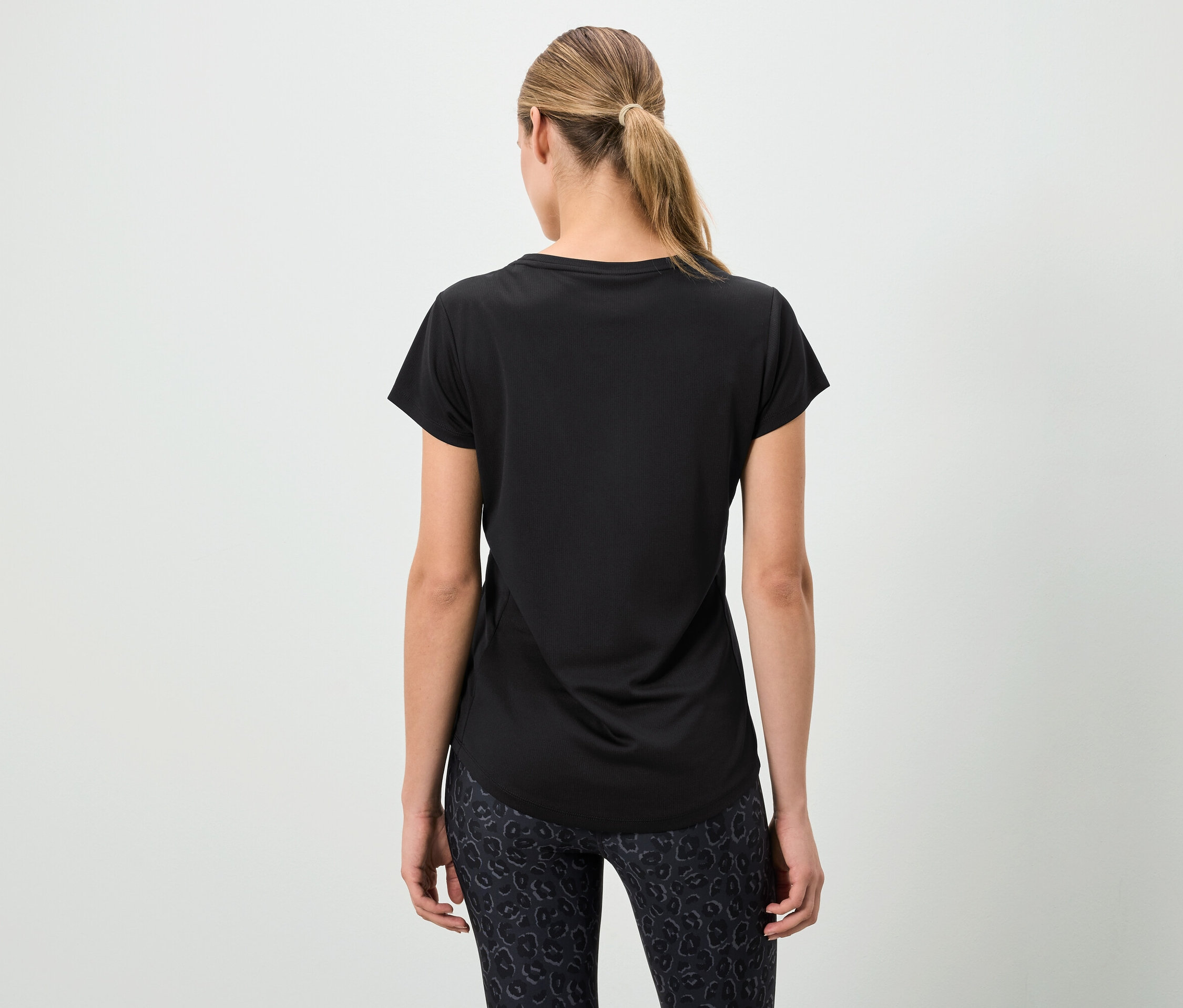 Frau von hinten trägt ein schwarzes T-Shirt und gemusterte Leggings.