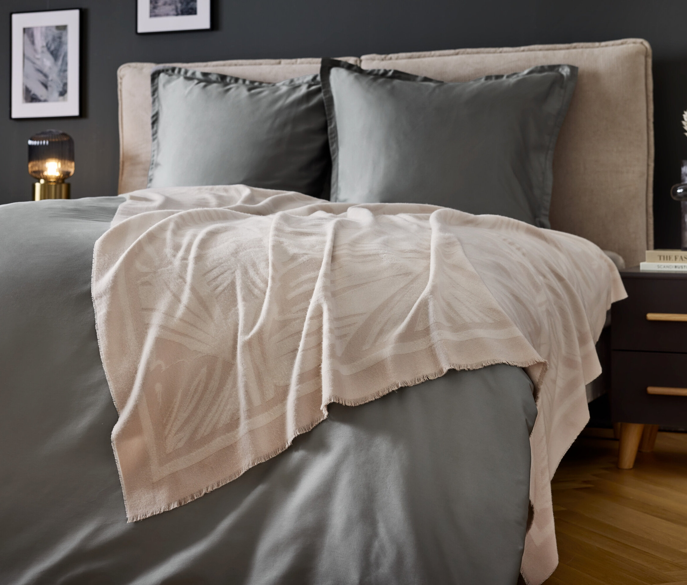 Schlafzimmer mit grauer Bettwäsche und beiger Decke mit Blattdruck.