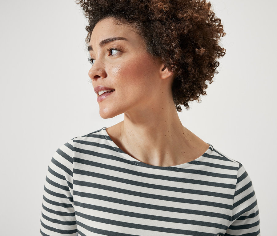 Porträt einer Frau mit kurzen lockigen Haaren. Sie trägt ein grün gestreiftes Halbarmshirt.