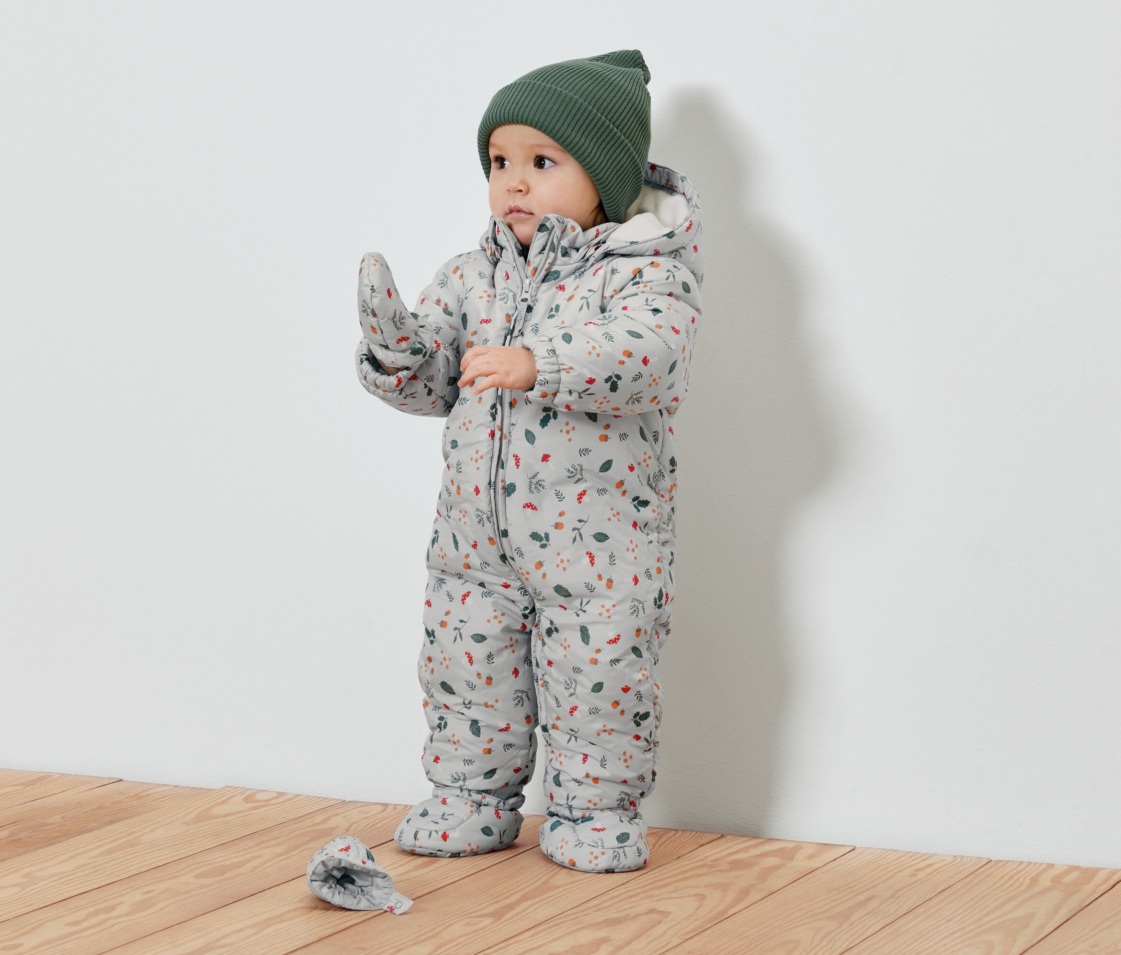 Kleinkind im floral gemusterten Schneeanzug und grüner Mütze.