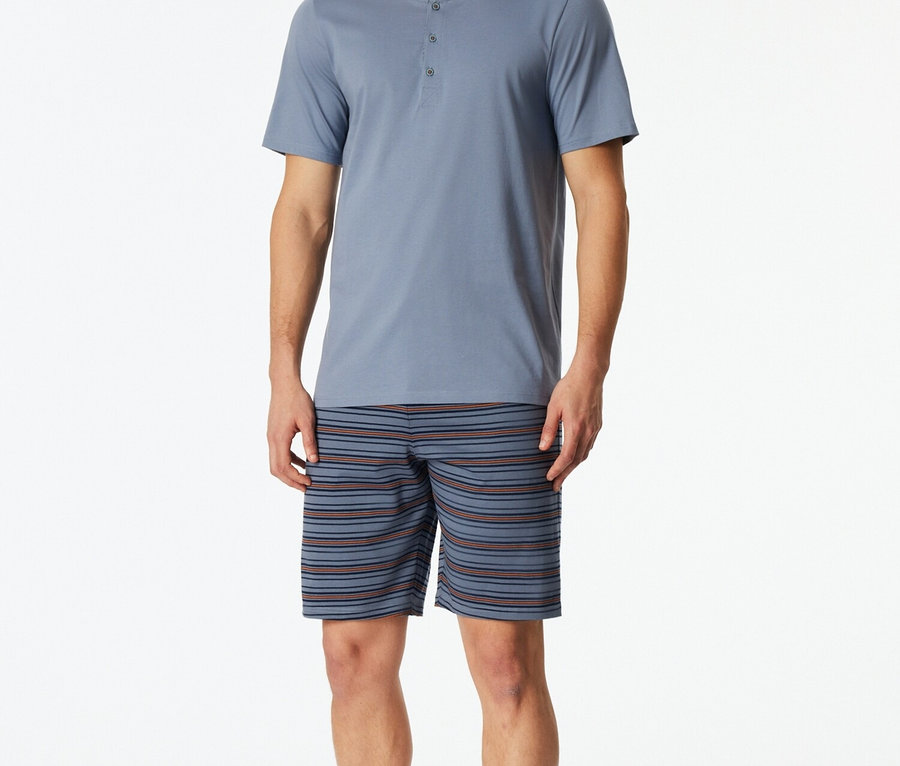 Mann im blauen Pyjama-Oberteil mit Knopfleiste und gestreiften Shorts.