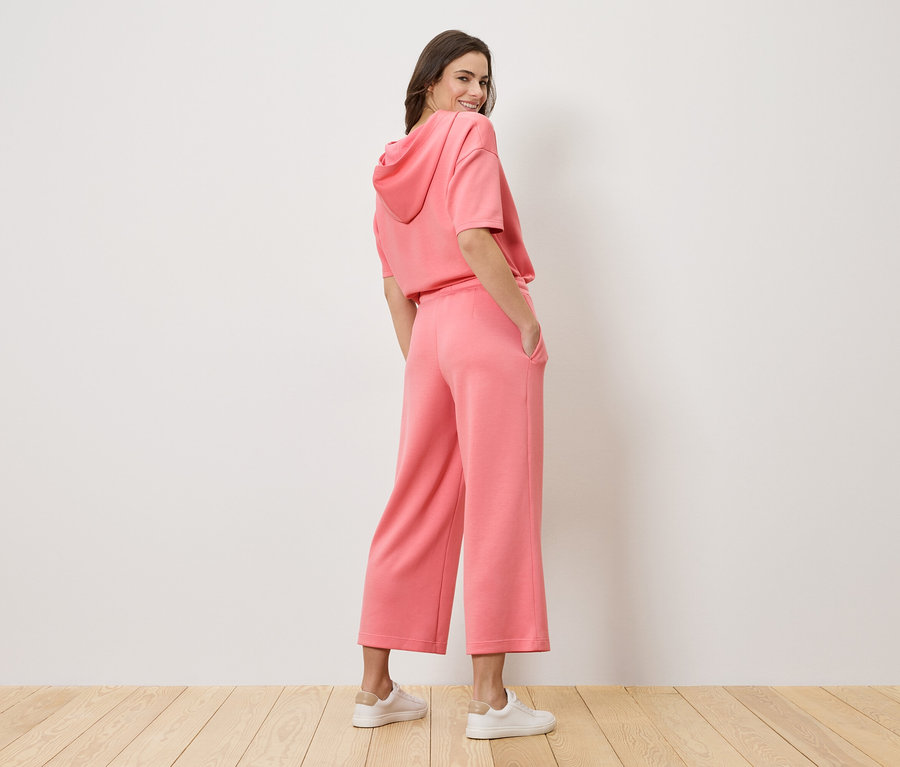 Frau mit Blick über die Schulter trägt einen rosa Hoodie und eine Culotte-Hose.