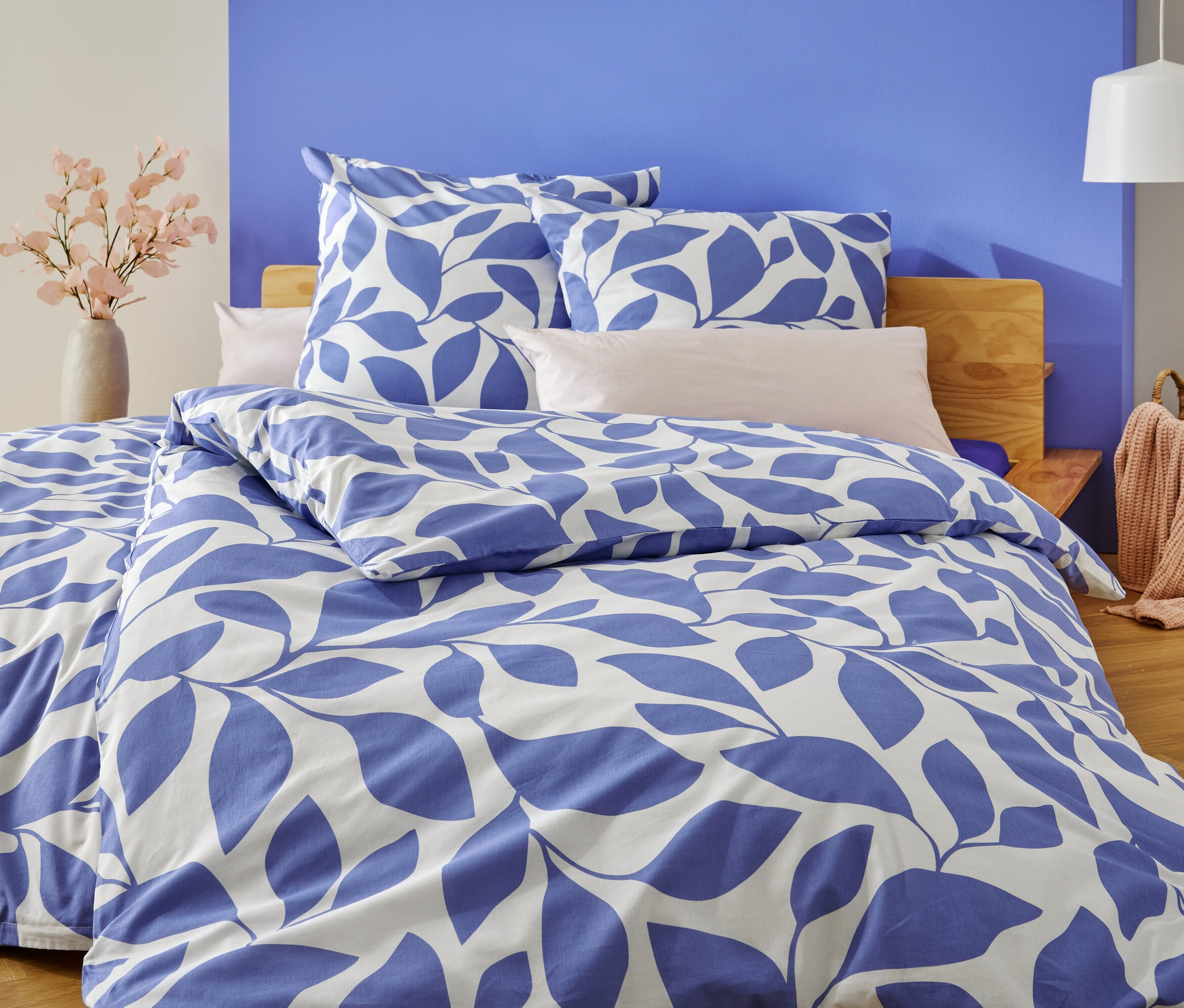 Ein Bett mit blau-weißer Blätterbettwäsche steht vor einer blau und weiß gestrichenen Wand.