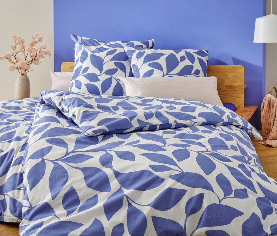 Ein Bett mit blau-weißer Blätterbettwäsche steht vor einer blau und weiß gestrichenen Wand.