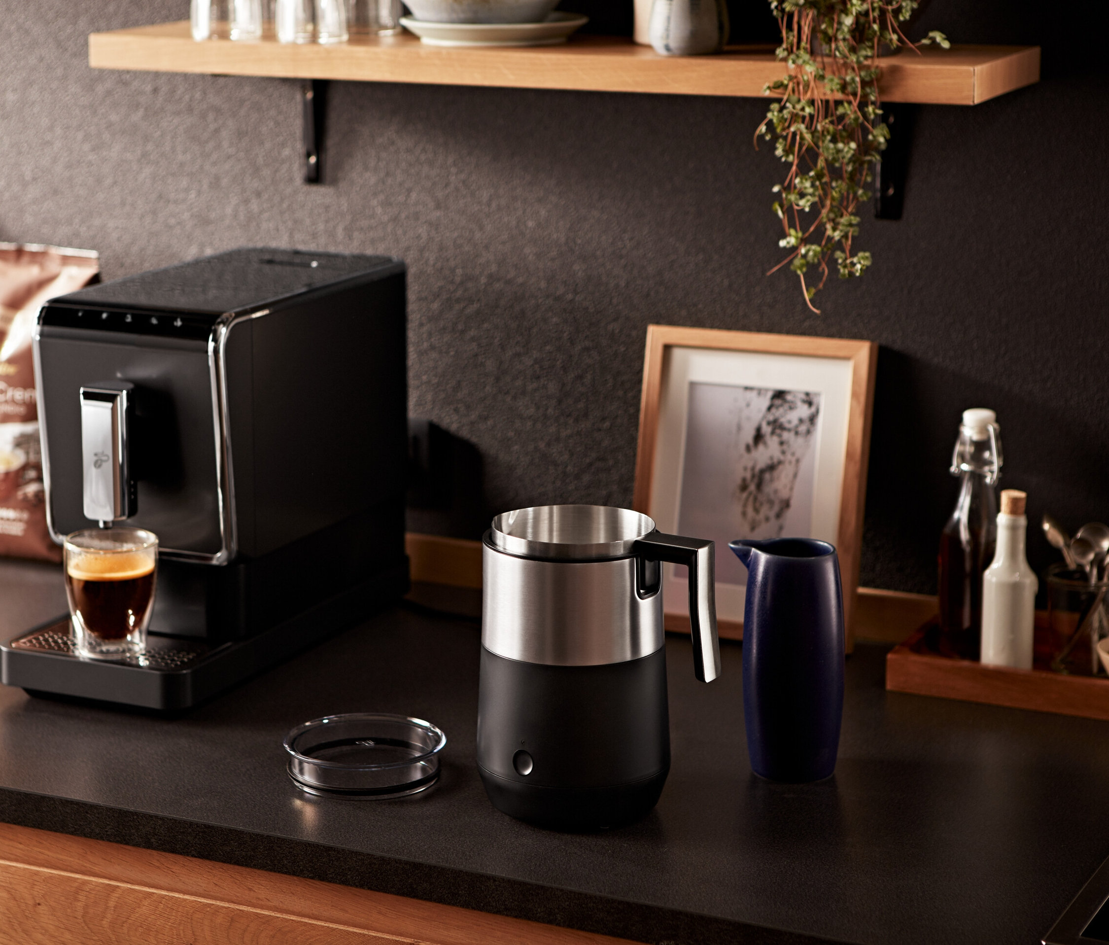 Espressomaschine gießt Kaffee in ein Glas neben einem Induktions-Milchaufschäumer, schwarz.