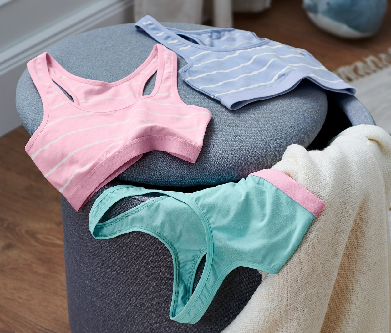 Drei Bustiers aus Bio-Baumwolle liegen auf einem grauen Hocker.