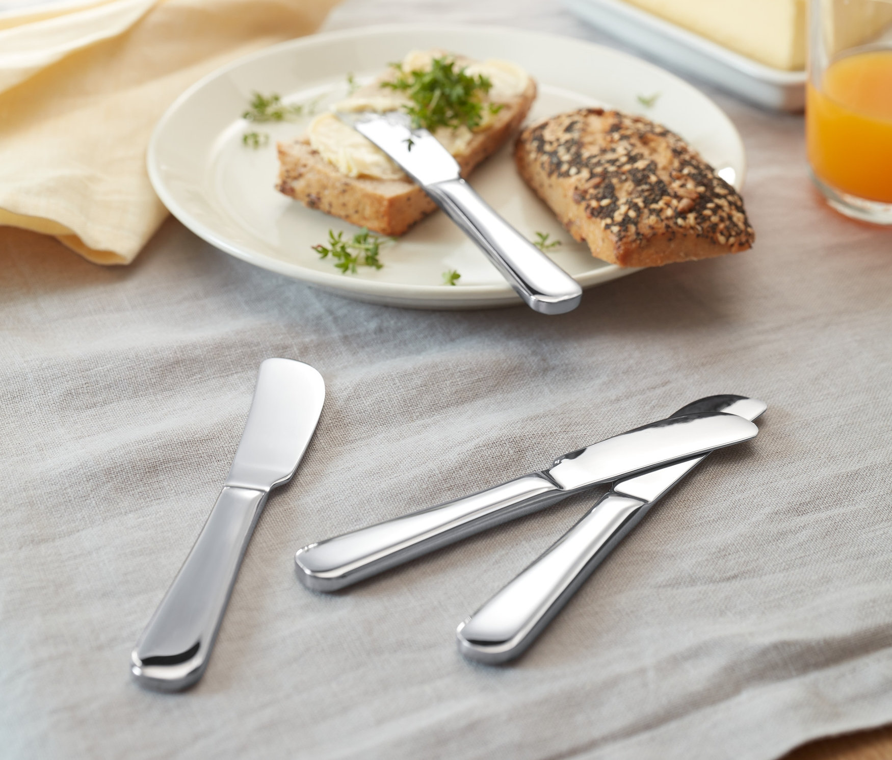 Auf einem Tisch liegen Brot mit Butter und 4 Buttermesser.