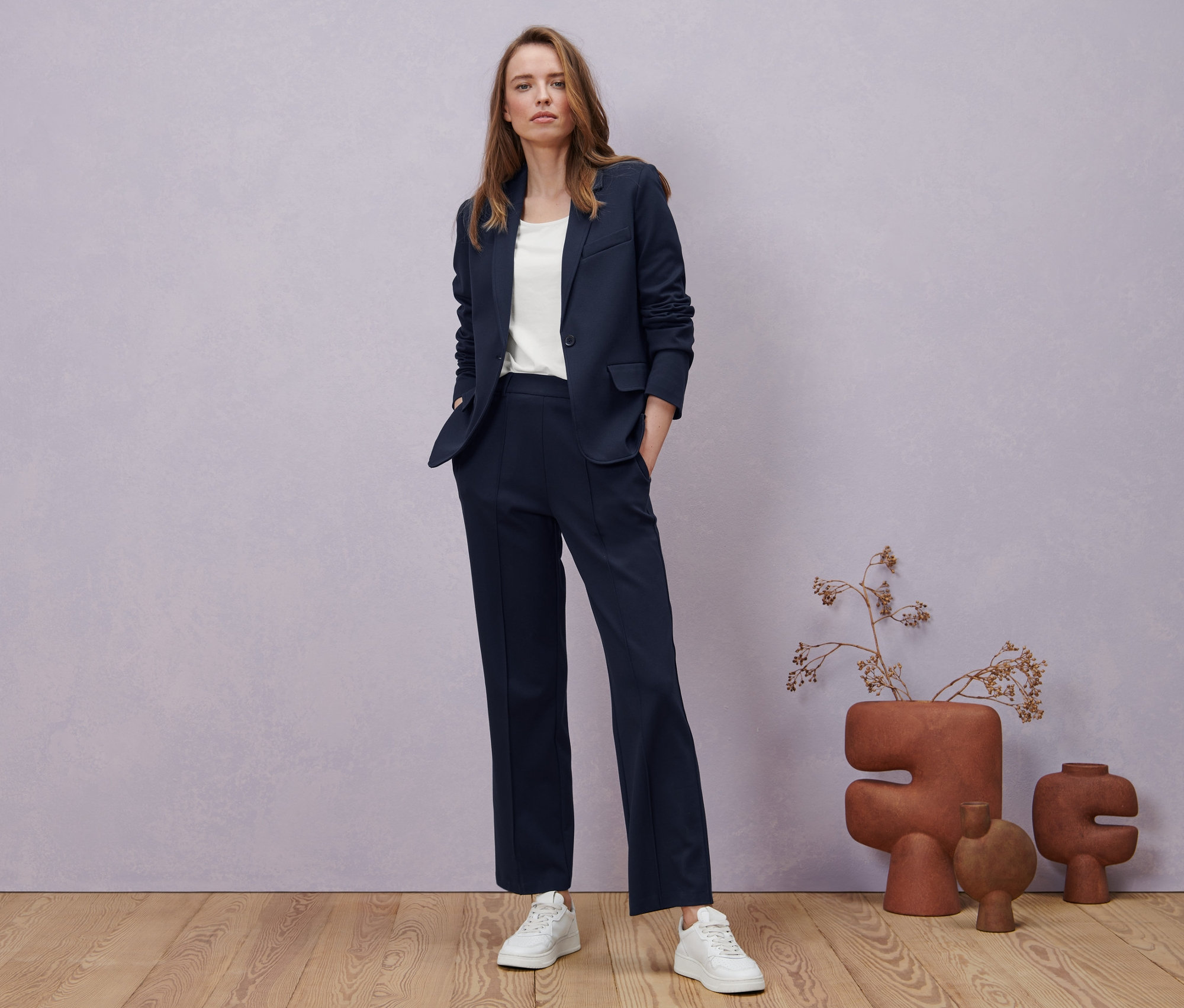 Eine Frau posiert in einer dunkelblauen Jerseyhose mit Biese, einem Jerseyblazer und einem weißen Halbarmshirt.