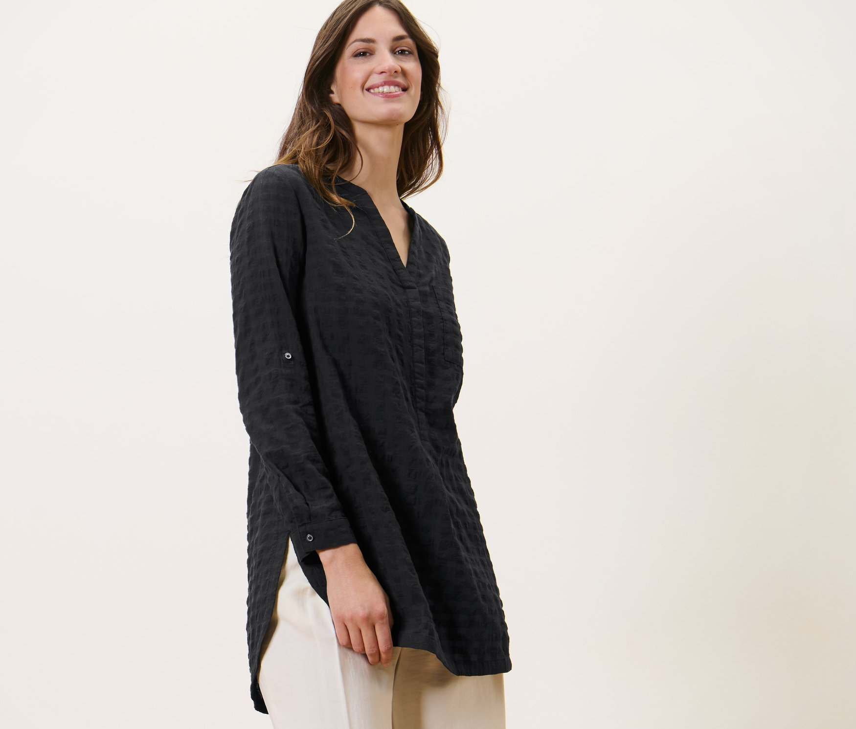 Frau trägt eine Longtunika mit Webstruktur und helle Hosen.