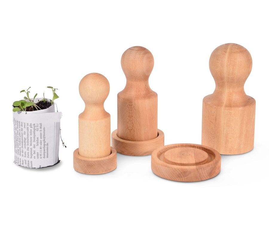 Drei Dobar 3 Papiertopf-Pressen aus Holz und ein Setzling in einem Papiertopf.