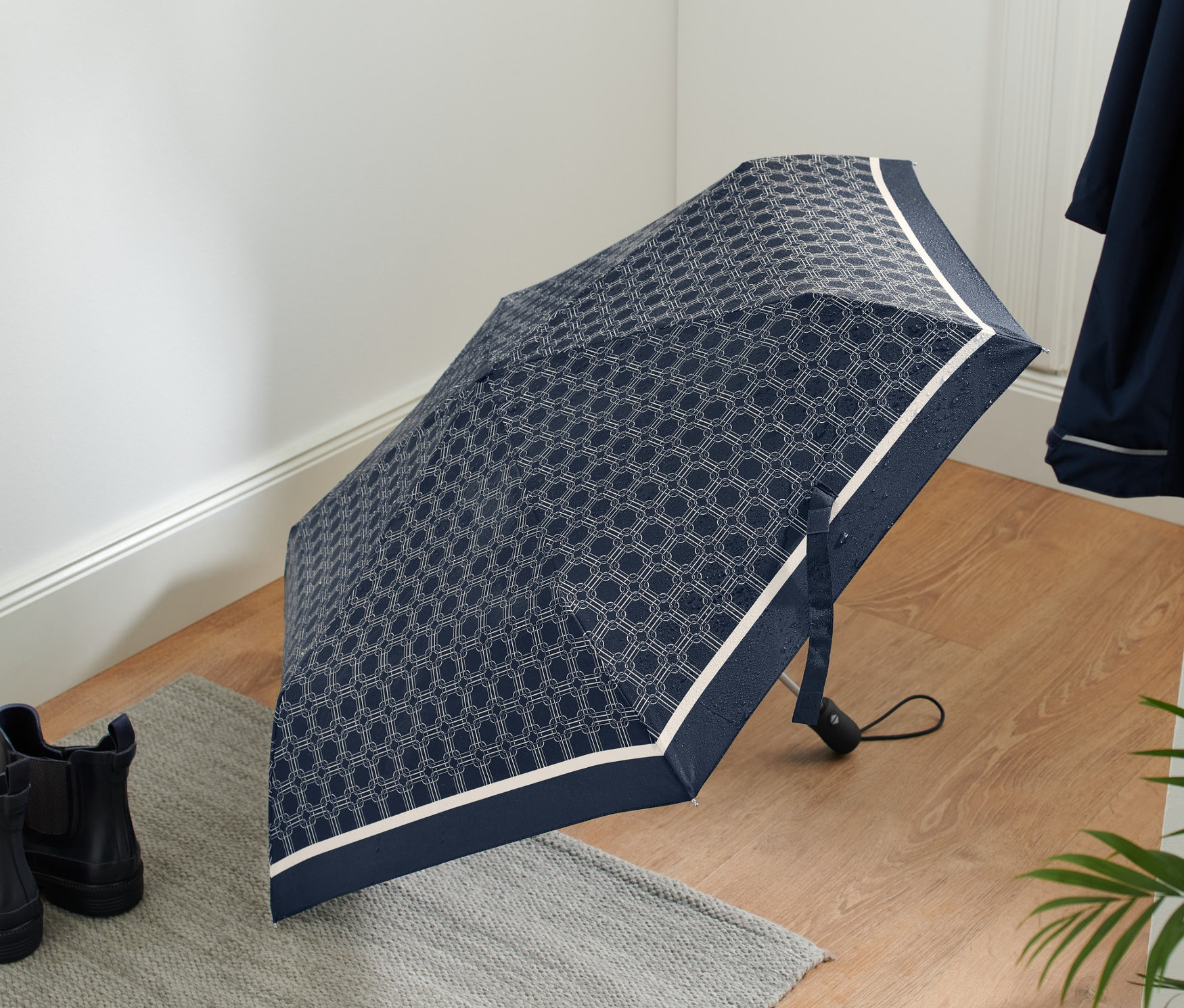 Ein geöffneter Automatik-Taschenschirm mit geometrischem Muster liegt auf dem Boden neben Stiefeln.