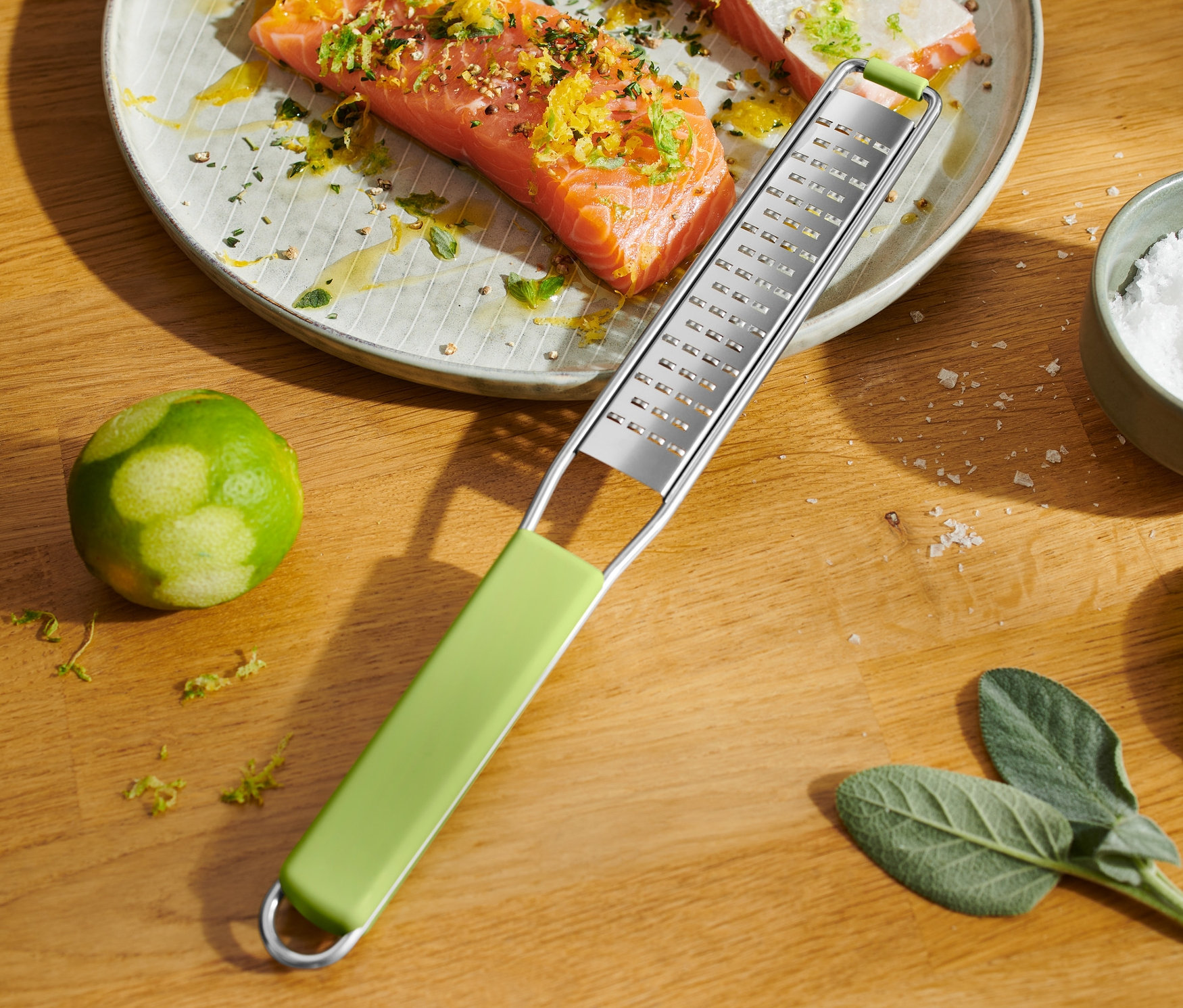 Lachs liegt auf einem Teller und ist mit Zitrusschalen bestreut. Daneben liegt eine feine Handreibe.