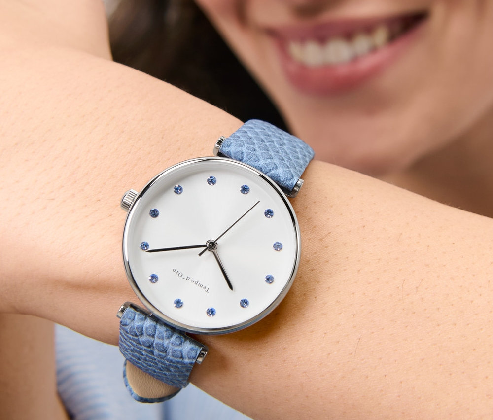 Lächelnde Frau trägt eine Armbanduhr mit Lederband und Kristallen am Handgelenk.