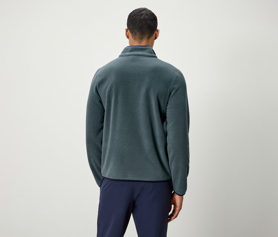 Mann von hinten mit grünem Fleecepullover und blauen Hosen.