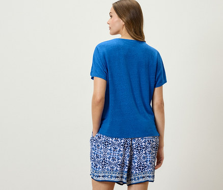 Frau posiert von hinten in kobaltblauem Shirt aus Leinenmix und blau-weißen Shorts.