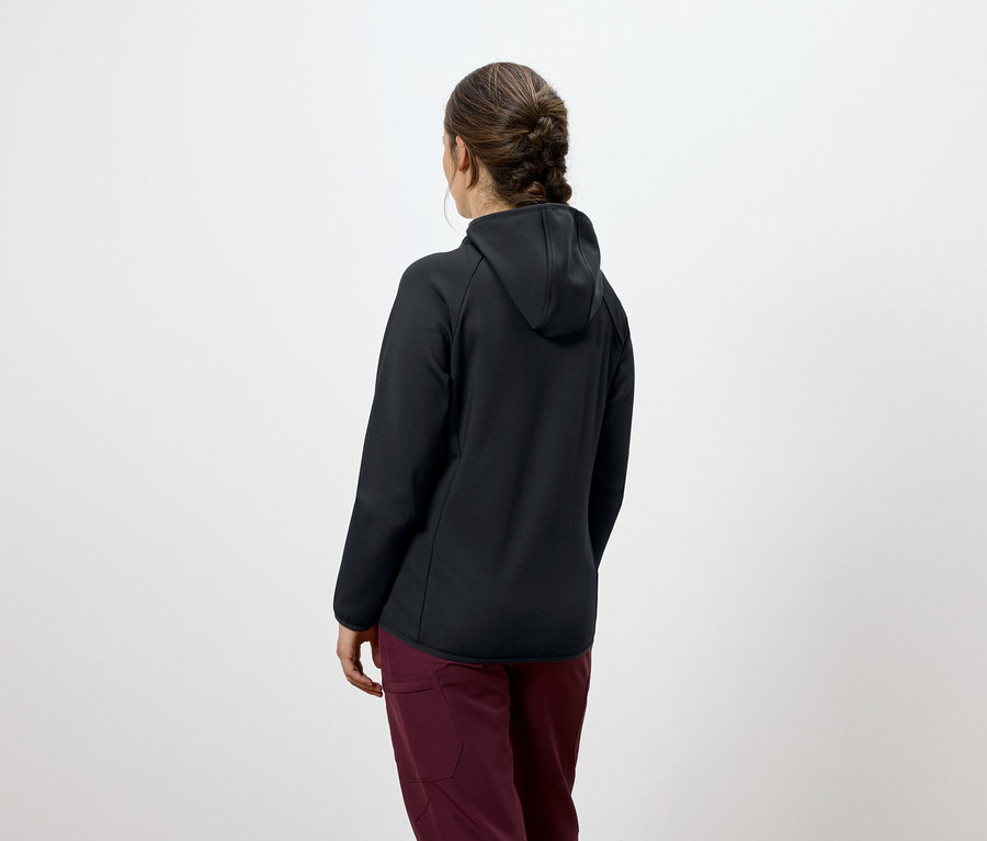 Rückansicht einer Frau mit braunen, geflochtenen Haaren, die eine schwarze Kapuzenjacke und eine bordeauxrote Hose trägt.